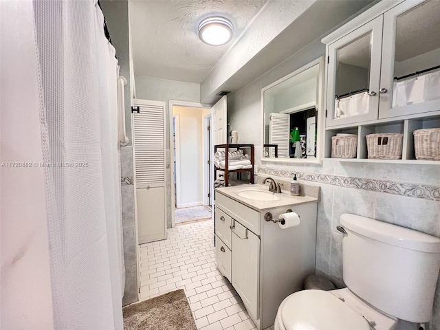 bathroom with vanity, tile patterned floors, toilet, a textured ceiling, and tile walls