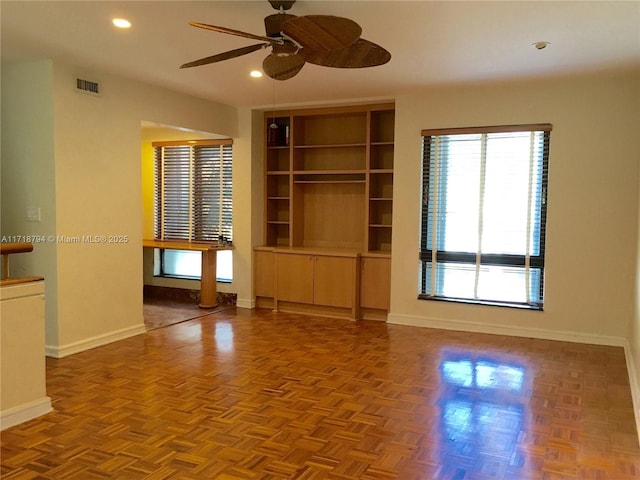 empty room featuring ceiling fan, built in features, and parquet flooring