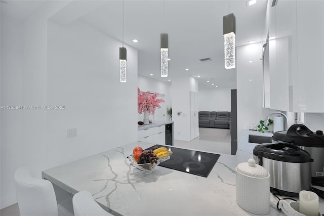 kitchen featuring pendant lighting, light stone counters, white cabinetry, and black electric stovetop