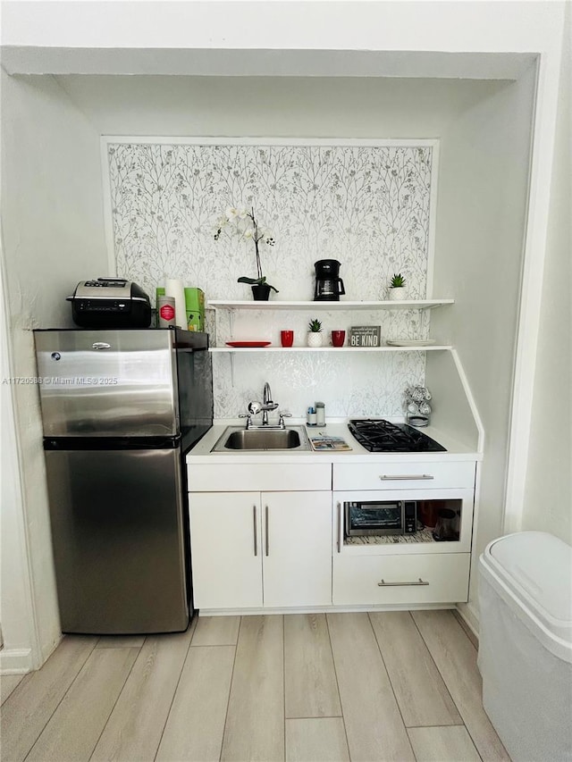 kitchen featuring black gas cooktop, sink, decorative backsplash, white cabinetry, and stainless steel refrigerator