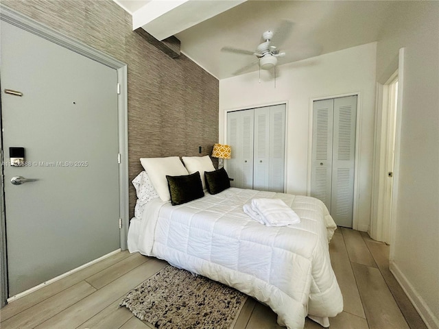 bedroom with light hardwood / wood-style flooring, ceiling fan, and multiple closets