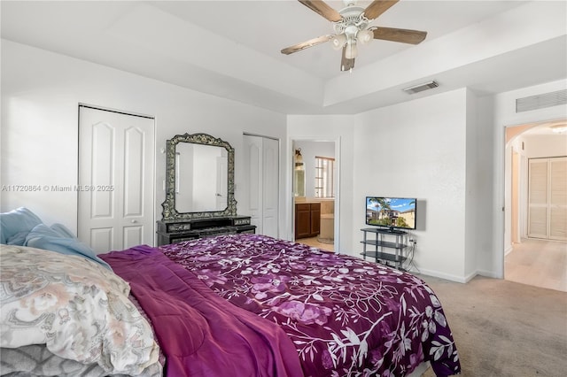 carpeted bedroom with connected bathroom, a raised ceiling, ceiling fan, and multiple closets