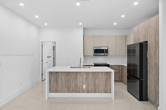 kitchen featuring range, black refrigerator, a center island with sink, and sink