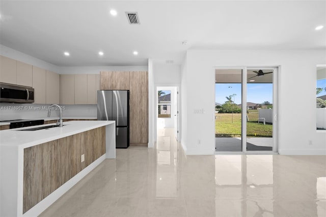 kitchen featuring ceiling fan, sink, stainless steel appliances, tasteful backsplash, and a kitchen island with sink