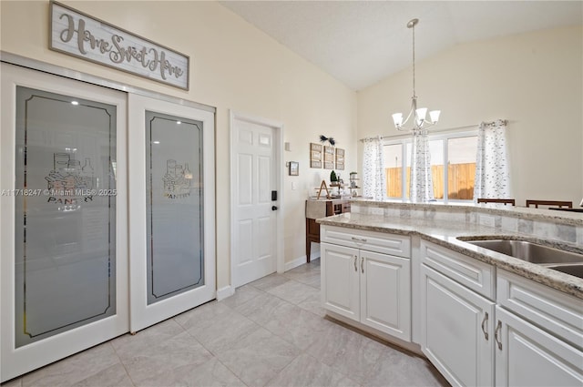 kitchen with an inviting chandelier, white cabinets, hanging light fixtures, vaulted ceiling, and light stone counters