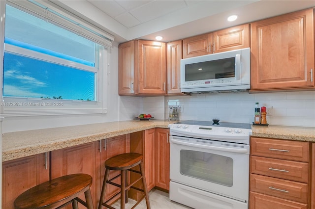 kitchen featuring a breakfast bar, light stone countertops, white appliances, and tasteful backsplash