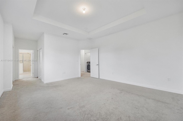 empty room with washer / dryer, light carpet, and a tray ceiling