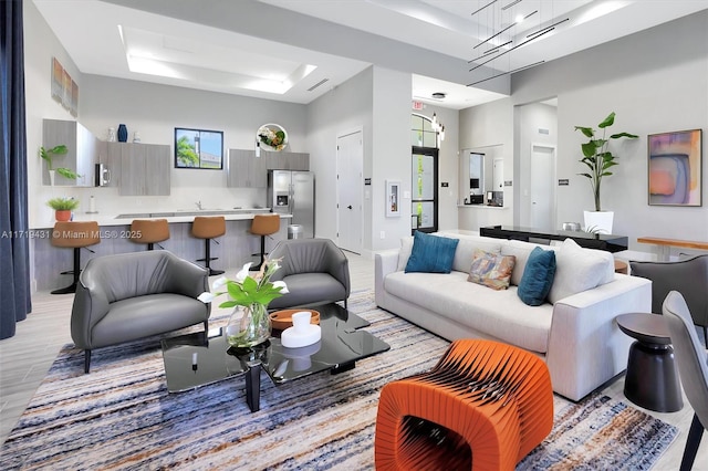 living room featuring a towering ceiling, light hardwood / wood-style floors, a raised ceiling, and a chandelier