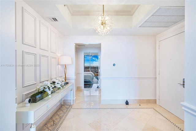 corridor featuring light tile patterned floors, a tray ceiling, ornamental molding, and a notable chandelier