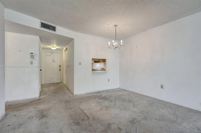 carpeted spare room featuring a textured ceiling and a notable chandelier