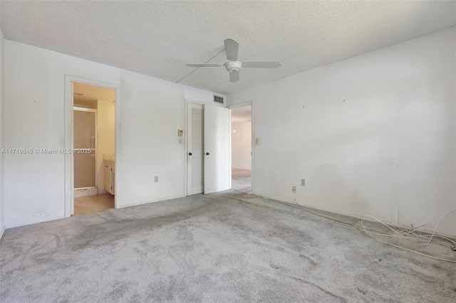 unfurnished bedroom featuring a textured ceiling, light colored carpet, ensuite bath, and ceiling fan