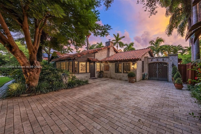 mediterranean / spanish-style home featuring a tiled roof, fence, a chimney, and stucco siding