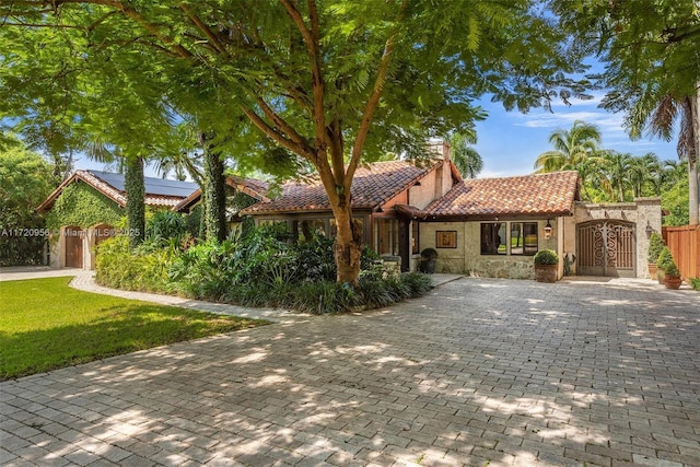 mediterranean / spanish house featuring a tile roof, fence, stone siding, driveway, and a front lawn