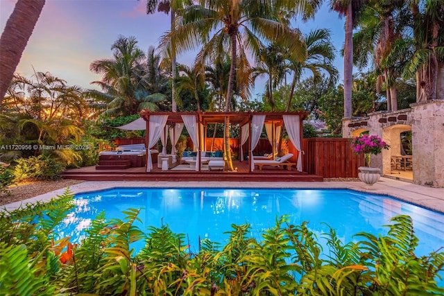 pool at dusk featuring fence, a jacuzzi, and an outdoor pool