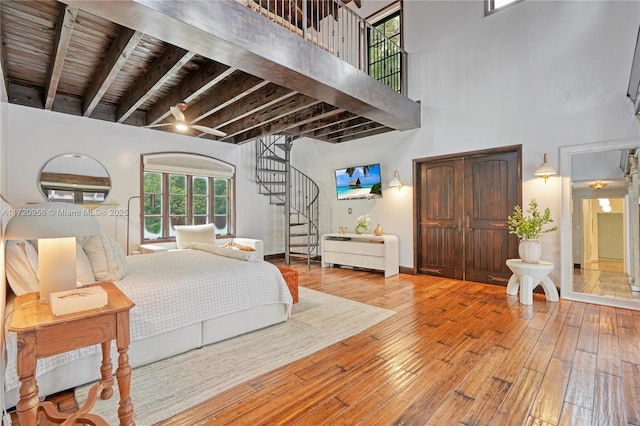 bedroom featuring light wood-type flooring, a high ceiling, baseboards, and beam ceiling