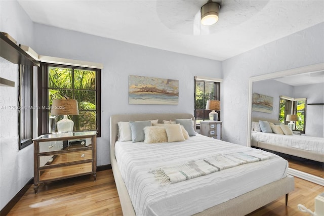 bedroom featuring a ceiling fan, baseboards, wood finished floors, and a textured wall