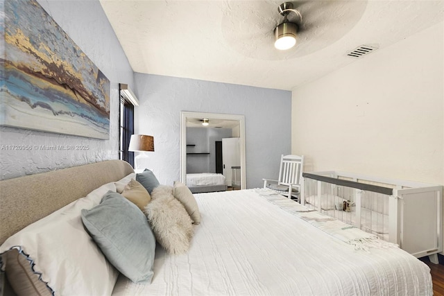 bedroom featuring visible vents, a textured wall, a ceiling fan, a textured ceiling, and wood finished floors