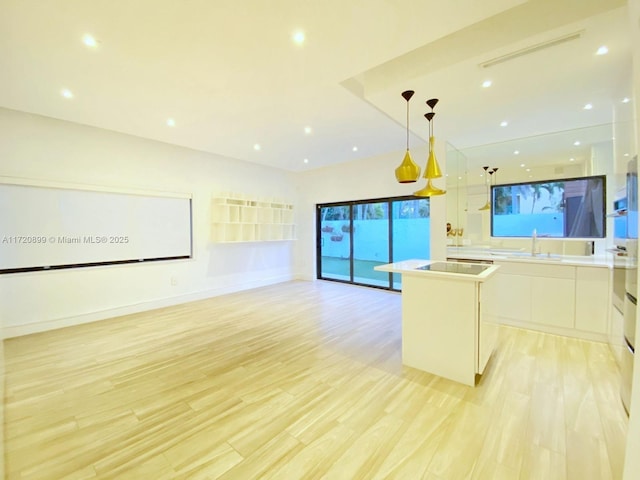 kitchen with a center island, sink, hanging light fixtures, white cabinets, and light wood-type flooring