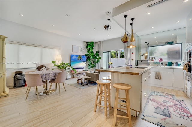 kitchen with light wood-type flooring, a breakfast bar, white cabinets, a kitchen island, and hanging light fixtures