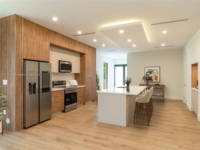 kitchen with a kitchen breakfast bar, a center island, light hardwood / wood-style floors, and appliances with stainless steel finishes