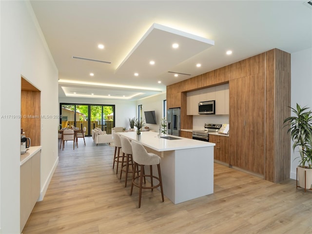 kitchen with a large island, sink, light hardwood / wood-style floors, a breakfast bar, and appliances with stainless steel finishes