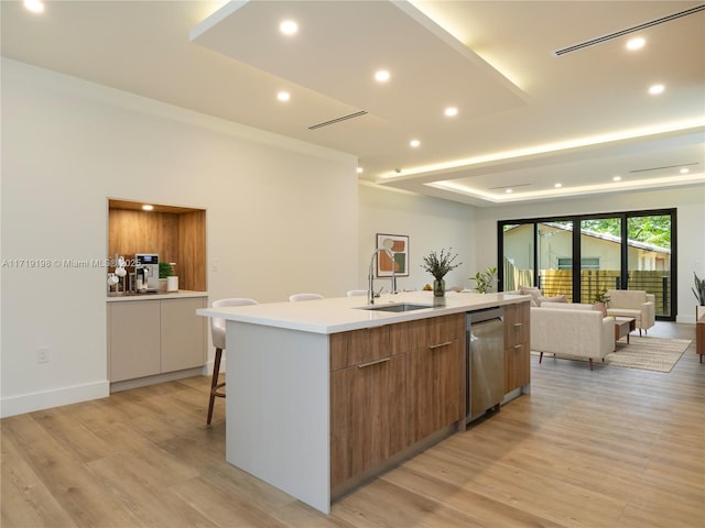 kitchen featuring a tray ceiling, sink, a spacious island, and light wood-type flooring