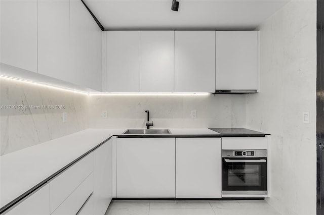 kitchen with black electric cooktop, stainless steel oven, white cabinets, and sink