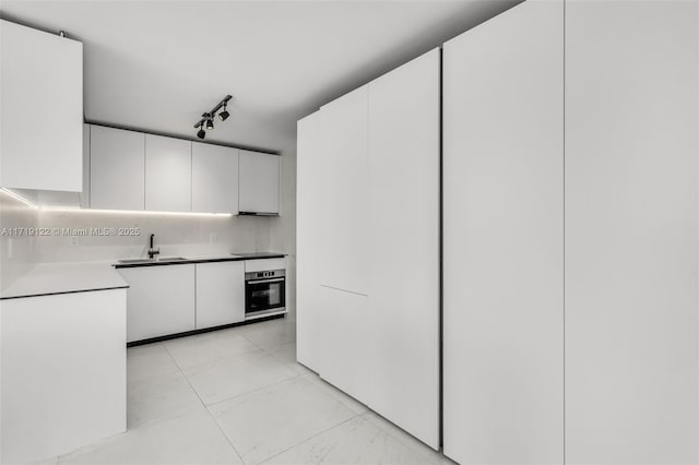 kitchen featuring sink, rail lighting, white cabinetry, and stainless steel oven