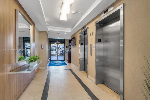 hallway with elevator, a tray ceiling, and light tile patterned flooring