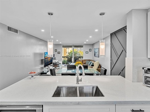 kitchen featuring light stone countertops, sink, white cabinets, and pendant lighting