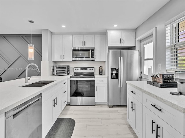 kitchen featuring white cabinetry, sink, light stone counters, decorative light fixtures, and appliances with stainless steel finishes