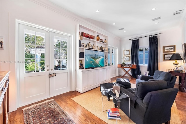 living room with french doors, ornamental molding, and light wood-type flooring