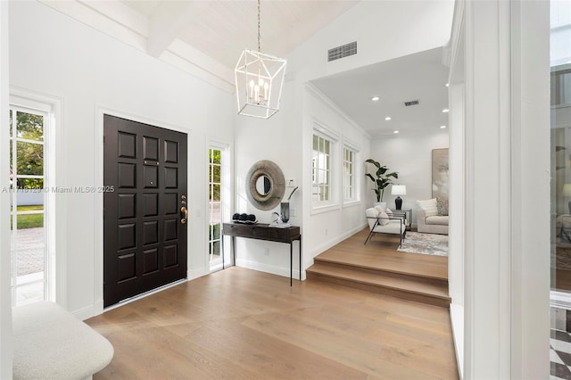 foyer entrance featuring plenty of natural light, lofted ceiling with beams, a notable chandelier, and light hardwood / wood-style flooring