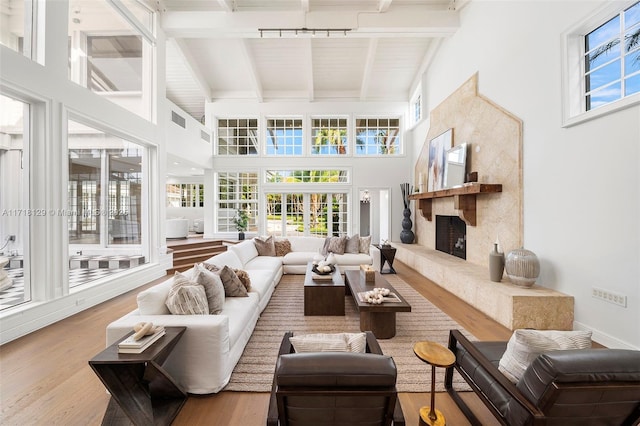 living room featuring a fireplace, wood-type flooring, a towering ceiling, and beamed ceiling