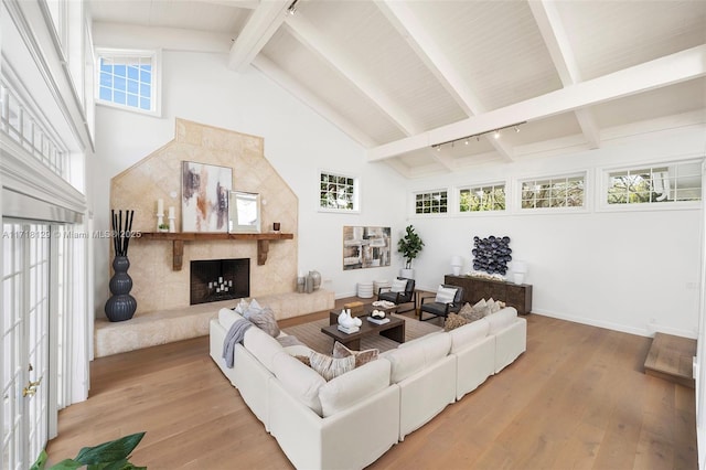 living room with track lighting, high vaulted ceiling, light hardwood / wood-style flooring, a premium fireplace, and beamed ceiling