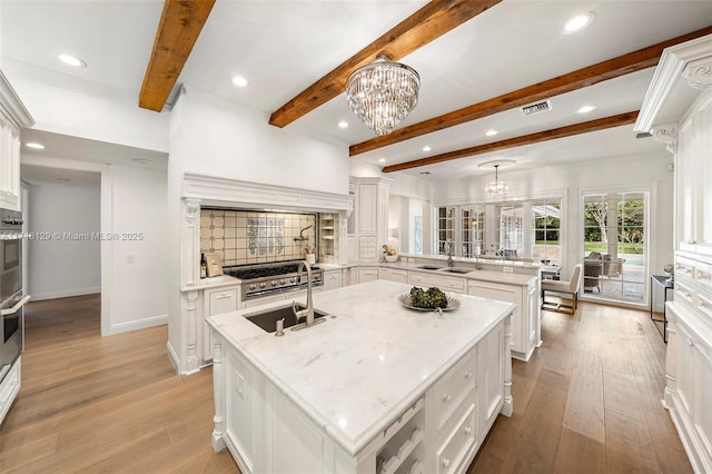 kitchen featuring sink, kitchen peninsula, pendant lighting, a center island with sink, and white cabinets