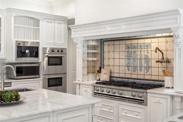 kitchen featuring light stone countertops, sink, stainless steel appliances, backsplash, and white cabinets