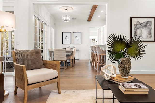 living area featuring beamed ceiling, a notable chandelier, and hardwood / wood-style flooring