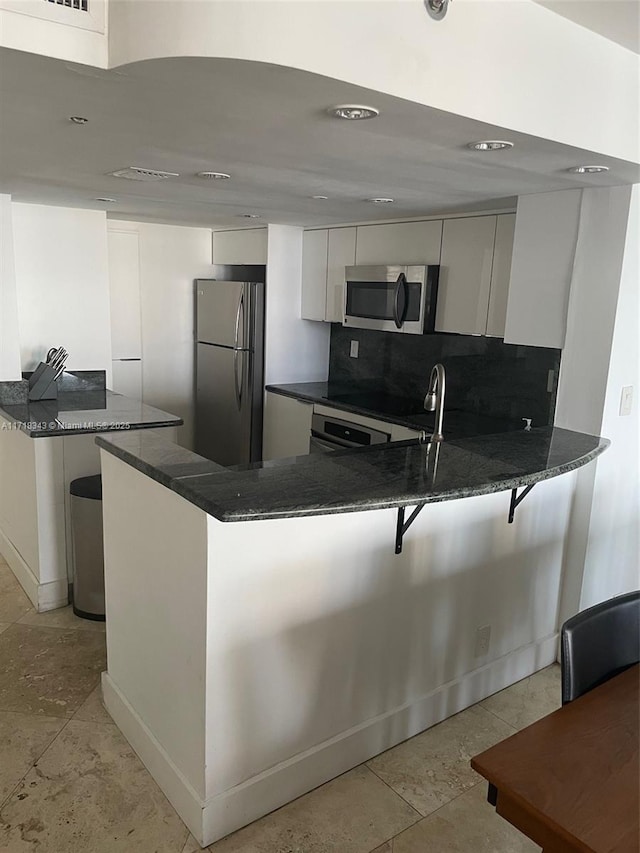 kitchen featuring backsplash, kitchen peninsula, white cabinets, and stainless steel appliances