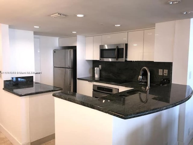 kitchen with kitchen peninsula, appliances with stainless steel finishes, sink, dark stone countertops, and white cabinets