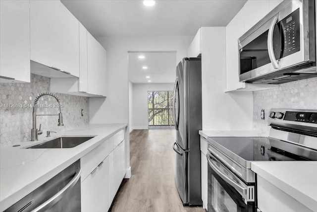 kitchen with tasteful backsplash, stainless steel appliances, sink, white cabinets, and light hardwood / wood-style floors