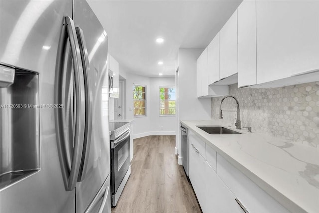 kitchen with white cabinetry, sink, stainless steel appliances, light stone counters, and backsplash