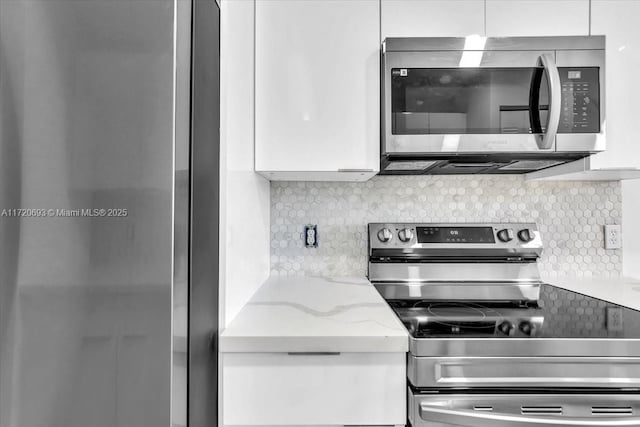 kitchen with backsplash, light stone counters, white cabinets, and appliances with stainless steel finishes