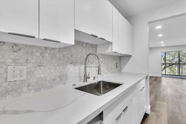 kitchen with white cabinetry, sink, light stone countertops, light hardwood / wood-style flooring, and backsplash