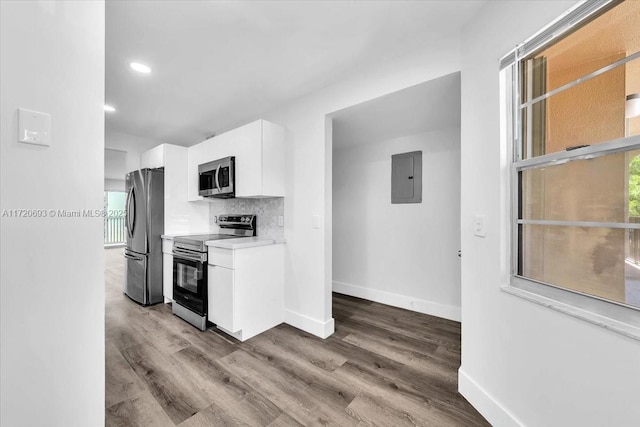 kitchen with electric panel, white cabinets, hardwood / wood-style flooring, appliances with stainless steel finishes, and tasteful backsplash