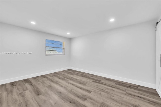 unfurnished room with a barn door and wood-type flooring