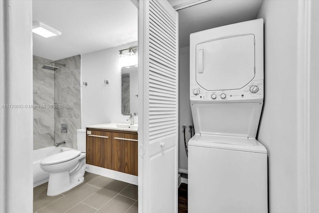 full bathroom featuring tile patterned floors, vanity, tiled shower / bath combo, stacked washer and clothes dryer, and toilet