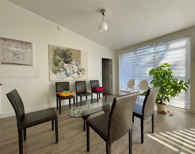 dining room featuring light hardwood / wood-style floors, a textured ceiling, and vaulted ceiling