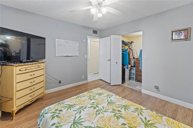 bedroom with a textured ceiling, ceiling fan, a spacious closet, light hardwood / wood-style floors, and a closet