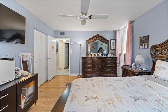 bedroom with ceiling fan, light hardwood / wood-style floors, a textured ceiling, and a closet